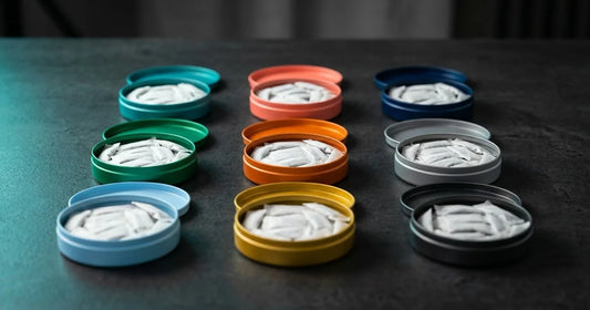 Colorful energy pouch tins open on dark surface showing white caffeine pouches inside